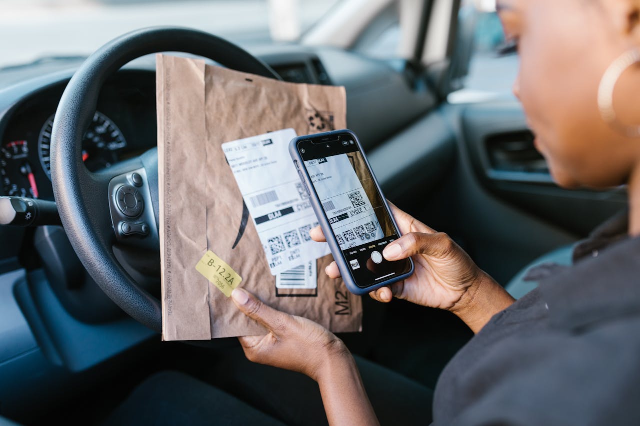 Services-01 Close-up of a courier in a car scanning a package label with a smartphone for delivery service.
